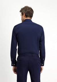 Granatowa koszula wizytowa z długimi rękawami, gładką fakturą, mankietami na guziki i usztywnianym kołnierzykiem; noszona z dopasowanymi spodniami.