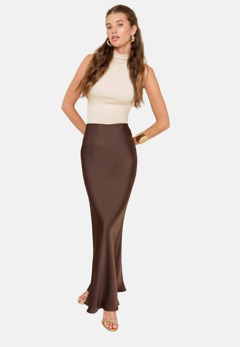 Bruine satijnen maxi rok met een getailleerde taille, gecombineerd met een beige mouwloos top. Gladde textuur en elegante silhoeët. Gouden armband accent.