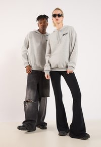Gray hoodies with front pockets and an embroidered logo, paired with black flared pants. Both wear black footwear and sunglasses.