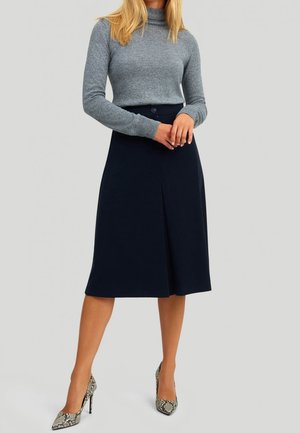 Marineblauer A-Linien-Rock mit einer Vorderfalte, kombiniert mit einem hellgrauen, figurbetonten Rollkragenpullover und gemusterten High-Heels. Glatte Texturen und klare Linien.