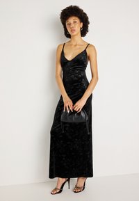 Melnas samta maxi kleita ar plānām siksnām, ar smalku ziedu rakstu. Apvienota ar mazu melnu somiņu un siksnu augstpapēžu sandālēm.