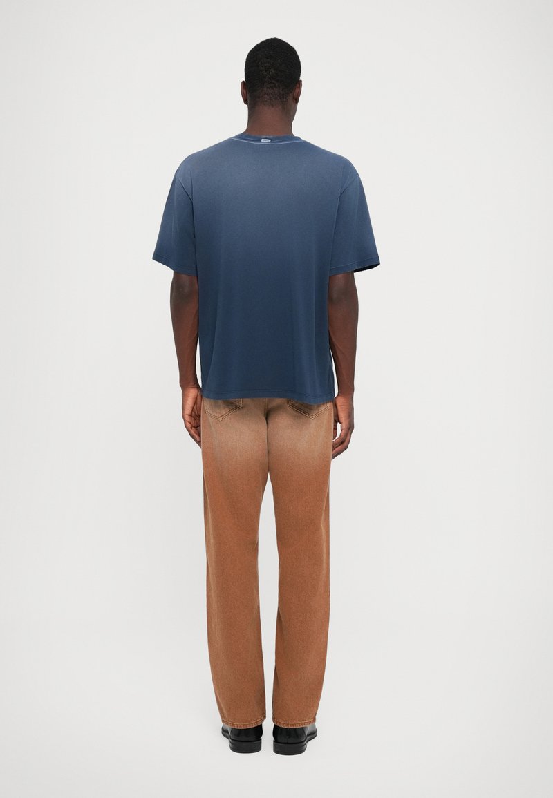 Marineblaue T-Shirt mit rundem Ausschnitt, kurzen Ärmeln und lockerer Passform, kombiniert mit hellbraunen tapered Hosen und schwarzen Schuhen.