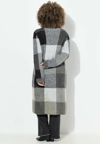 Dlouhý cardigan s kostkovaným vzorem v odstínech černé, šedé a bílé. Vyrobený z měkkého materiálu, s pletenými manžetami a lemem. Design v uvolněném střihu.