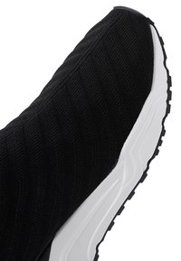 Black knitted fabric slip-on sneaker with thick white sole and textured black outsole.