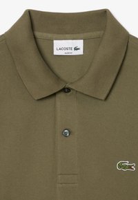 Olivovo zelená polo tričko s textúrovanou tkaninou, slim fit strihom, trojzápadkovou légou a malým vyšitým logom Lacoste na hrudi.