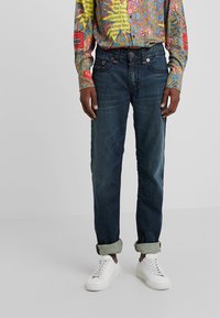 Mörkblå jeans med rak passform, som har en klassisk femfickdesign och uppvikt fåll, tillsammans med vita sneakers.