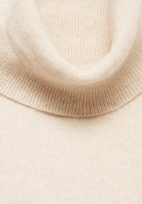 Beige coltrui met een zachte, geribbelde textuur en een brede hals. De stof lijkt lichtgewicht en iets rekbaar.