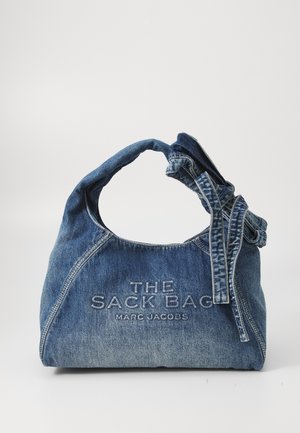 Denim skuldertaske med en rund top, knyttet rem og broderet "THE SACK BAG" og "MARC JACOBS." Har en blød, struktureret overflade.