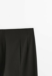 Pantalon noir taille haute avec devant plat et coutures propres, montré de la taille jusqu'au milieu de la cuisse sur un fond blanc.