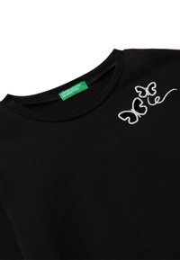 Černé tričko s kulatým výstřihem a bílými vyšívanými motivy motýlů blízko ramene, s zelenou nášivkou "United Colors of Benetton" uvnitř límce.
