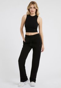Black ribbed crop top paired with black joggers featuring side pockets, drawstring waist, and subtle logo detailing. Worn with white sneakers.