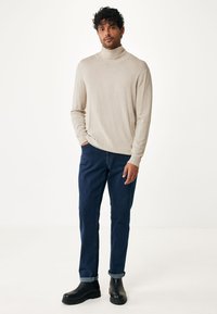 Pullover a collo alto beige realizzato in tessuto morbido, abbinato a jeans di denim blu scuro. Stivaletti neri alla caviglia con suola spessa completano l'outfit.