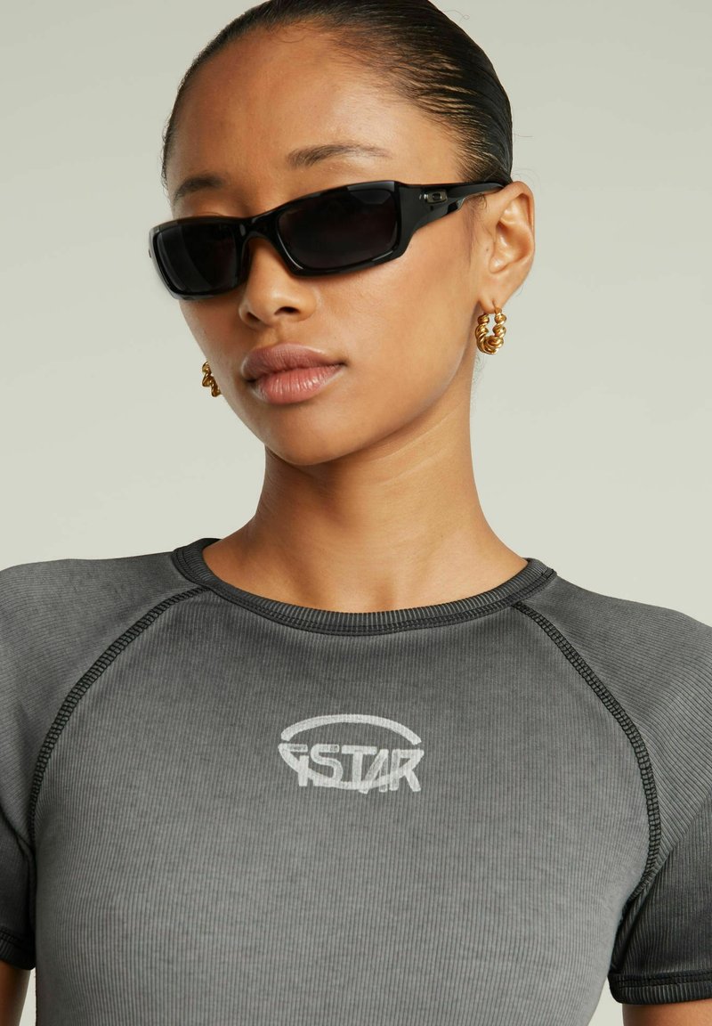 Top sportivo grigio a coste con maniche corte e scollatura rotonda. Presenta un logo bianco sul petto e cuciture nere a contrasto.