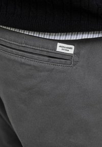 Szare bawełniane spodnie z detalem tylnej kieszeni, z metką "JACK & JONES EST. 1990" i subtelnymi akcentami przeszycia.