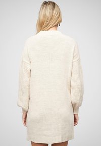 Krémově béžové oversized pletené šaty se strukturovanými balónovými rukávy a žebrovanými detaily. Měkká, lehká tkanina s uvolněným střihem.