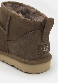 Bottine en suede marron avec une doublure en fourrure douce, forme arrondie, semelle plate en caoutchouc et logo UGG brodé sur le côté.