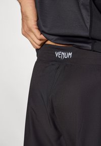 Fekete atlétikai rövidnadrág sima, rugalmas anyagból, fehér "Venum" logóval díszített derékpánttal és oldalsó varrás részlettel.
