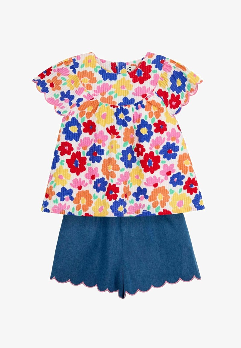 Lillelilledega pastelltoonides lühikarvaline pluus tekstureeritud kangast ja lainelise äärisega, kombineeritud tumepruunide teksashortsidega.