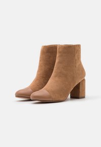 Bottes courtes en daim marron avec un bout en cuir lisse couleur tan, tige courte et talon bloc. Design classique pour une tenue décontractée à semi-formelle.