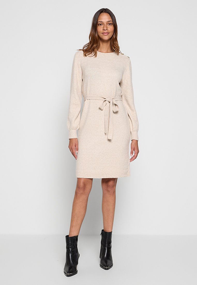Robe en tricot beige avec des manches longues, un col rond et une ceinture à la taille. Présente des boutons décoratifs sur l'épaule et une silhouette droite.