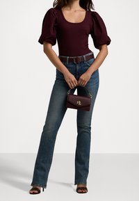 Burgundy puffärmad bodysuit, blå utsvängda jeans och svarta klacksandaler. Modellen håller en liten bourgogne kviltad handväska med ett guldinslag.