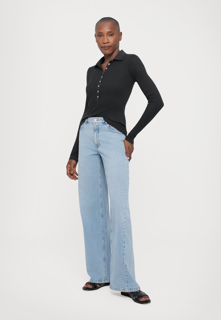 Black long-sleeve polo shirt with button placket paired with light blue wide-leg jeans. Flat black sandals complete the look.