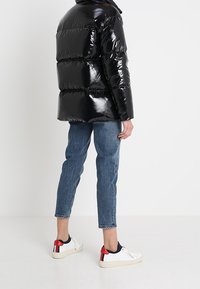 Černá lesklá péřová bunda s horizontálními pruhy, spárovaná s světle modrými džíny a bílými teniskami s červenými akcenty.