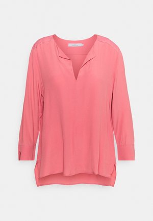 Blusa rosa de manga larga con corte en V, ajuste holgado, aberturas laterales y puños con botones, mostrada sobre fondo blanco.