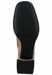 Suela de goma negra con ranuras texturizadas, parte superior beige con acabado suave, tacón bajo y detallado del logo en el tacón.