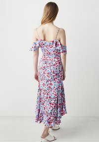 Robe maxi fleurie blanche avec des fleurs rouges et bleues. Caractérisée par des volants décolletés et un corsage ajusté, s'évasant au niveau de l'ourlet.