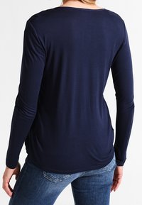Camiseta de manga larga azul marino, diseño ajustado con cuello redondo y textura suave. Presenta mangas enrolladas y un dobladillo curvado para mayor comodidad.