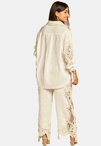 Blusa di lino bianca con dettagli in pizzo sulle maniche, abbinata a pantaloni di lino bianco a vestibilità ampia con intricati dettagli in pizzo lungo i lati.
