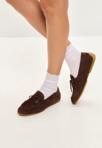 Brune ruskinds loafers med rund tå, snøredetalje og en let gummisål. Båret med hvide, bølgede ankelstrømper.