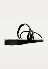 Svarta platta sandaler med en slät läderlook, med flätade remmar och en minimalistisk design, platt sula utan dekoration.