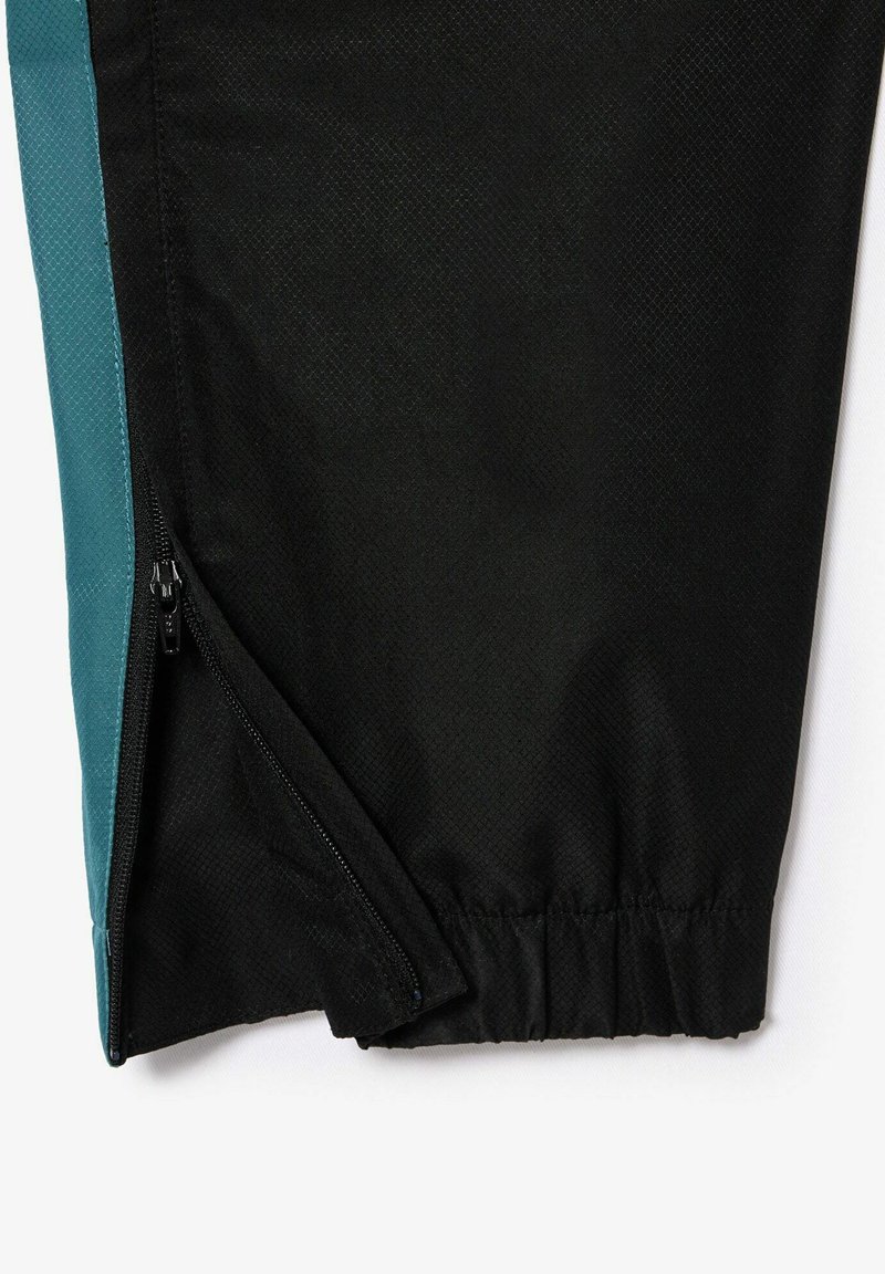 Pantalons capri de sport noirs et turquoise avec une fermeture éclair, tissu texturé et taille élastique. Détail de zip sur le côté visible.