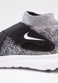 Černé a šedé tenisky Nike ve stylu ponožek s bílým logo swoosh na černém pásku a bílou podrážkou "Nike Free" na bílém pozadí.