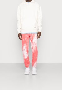 Vit hoodie med en framficka, i kombination med rosa tie-dye mjukisbyxor. Vita sneakers fulländar looken.