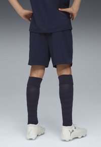 Marinblå idrottströja och shorts med randiga knä-långa strumpor. Skorna är ljusgrå med texturerad design och logotypdetaljer.