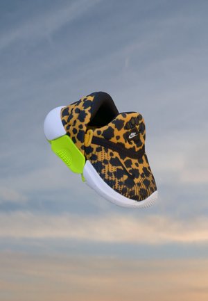 Chaussure enfant Nike slip-on avec motif léopard, maintien de talon vert fluo et semelle blanche sur fond de ciel.
