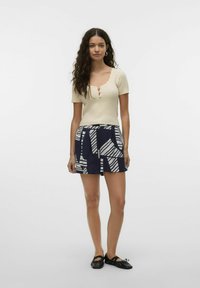 Haut beige tricoté avec un col en dentelle et des manches courtes, associé à un short bleu marine avec des motifs géométriques blancs et des poches. Ballerines noires.