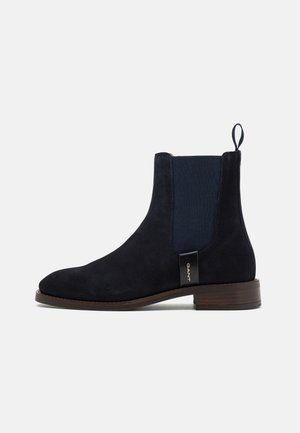 Navy suede Chelsea boot with elastic side panels, rounded toe, and pull tab. Features a wood-grain sole for stability.