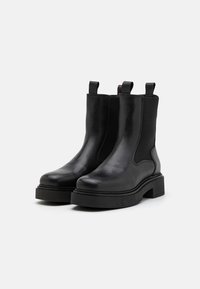 Sorte lær ankle boots med elastiske sidede paneler, flade gummisåler og trækflapper for nem påtagning. Minimalistisk design med glat tekstur.