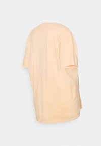 T-shirt de manga curta em pêssego pastel em algodão suave. Corte descontraído com decote redondo, bainha reta e detalhes de costura visíveis.