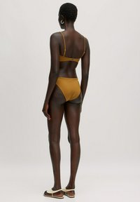 Mosterdgele bikini met een triangletop en een middenhoogte broekje, voorzien van verstelbare bandjes en een sluiting aan de achterkant. Nette textuur.