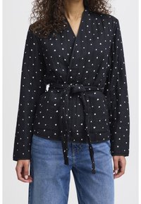 Haut enveloppant noir avec un imprimé cœur blanc, manches longues et taille nouée. Fabriqué à partir d'un tissu texturé, avec des détails de couture diagonale.