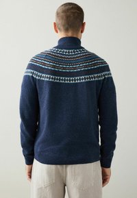 Marineblauer Strickpullover mit hohem Kragen, der ein mehrfarbiges Musterband über den Schultern aufweist. Weiche Textur und figurbetonte Bündchen.