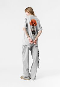 Camiseta gris de gran tamaño con un diseño de perro de dibujito en la parte posterior. Combinada con pantalones grises claros y sandalias; la textura parece suave.