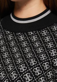 Maglione nero lavorato a maglia con motivo a disegni grigi che presenta un logo ripetuto. Scollo a girocollo a coste nero e grigio. Tessuto morbido.