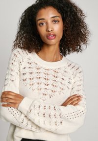 Kreminė megzta sv sweater, turinti atviras raštus, apvalią kaklą ir gumuotas rankoves. Minkšta tekstūra su laisvu siluetu.