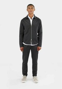 Donkergrijze zip-up jas met kraag, gecombineerd met bijpassende broek. Kenmerkt zich door een soepele textuur en een minimalistisch ontwerp. Gecombineerd met lichte sneakers.